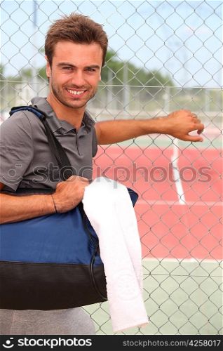 Smiling male tennis player with kitbag outside court