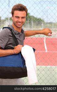 Smiling male tennis player with kitbag outside court