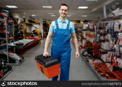 Smiling male worker in uniform buying toolbox in tool store. Choice of professional equipment in hardware shop, instrument supermarket. Male worker in uniform buying toolbox, tool store