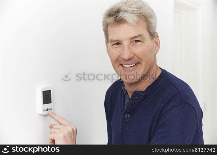 Smiling Man Adjusting Thermostat On Home Heating System
