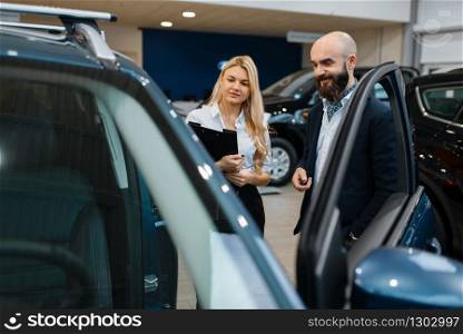 Smiling man and saleswoman in car dealership. Customer and seller in vehicle showroom, male person buying transport, auto dealer business. Smiling man and saleswoman in car dealership