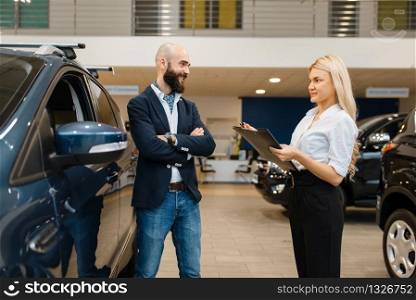 Smiling man and saleswoman in car dealership. Customer and seller in vehicle showroom, male person buying transport, auto dealer business. Smiling man and saleswoman in car dealership