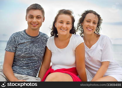 Smiling man and two young beautiful women sitting on beach