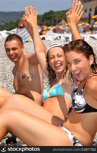 Smiling man and two young women on stony beach, lifted hands upwards