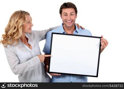 Smiling man and woman pointing at a blank board ready for your message