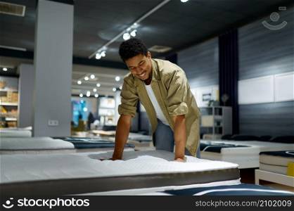 Smiling man choosing bed checking orthopedic mattress softness shopping at furniture store. Man choosing bed checking orthopedic mattress softness