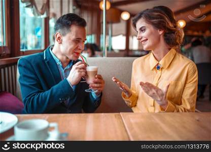 Smiling man drinks a cocktail from the straws against happy woman, restaurant on background. Love couple at romantic date
