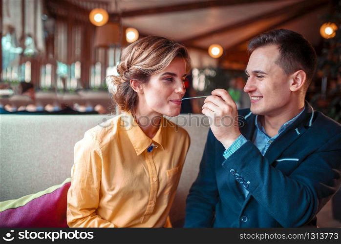 Smiling man feeding happy woman with a spoon in restaurant. Love couple at romantic dinner