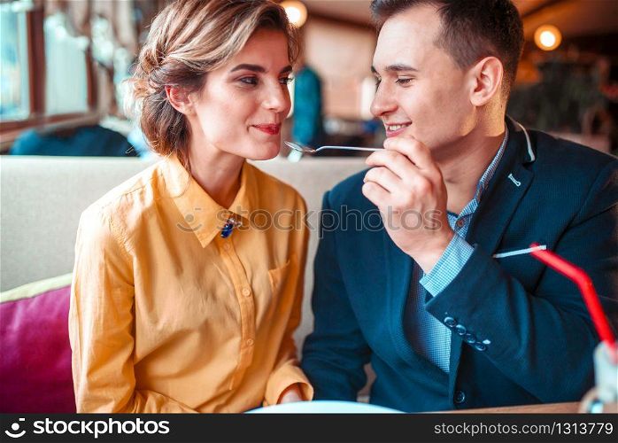 Smiling man feeding happy woman with a spoon in restaurant. Love couple at romantic dinner. Smiling man feeding woman with spoon in restaurant