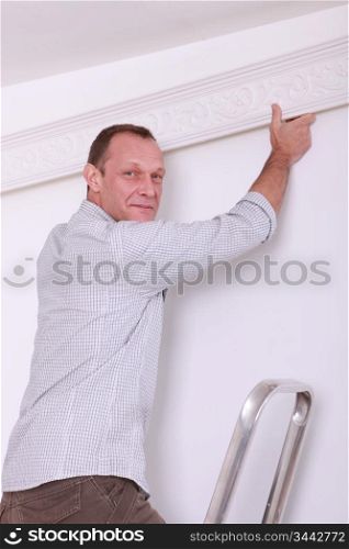 Smiling man fixing coving to a ceiling