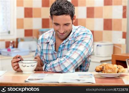 Smiling man having continental breakfast in his kitchen with a newspaper