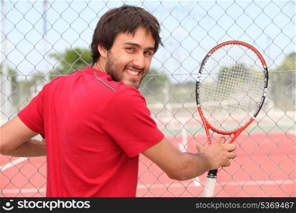Smiling man holding racquet by fence of municipal tennis court