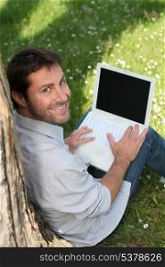 Smiling man in a park, using a laptop with the screen left blank to insert your image
