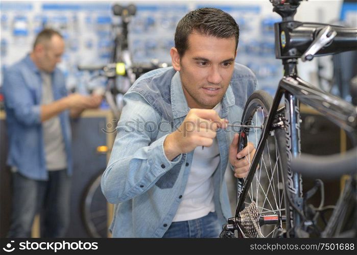 smiling man seller fixing bike wheel in sport hypermarket