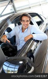 Smiling man sitting at the steering-wheel of brand new car