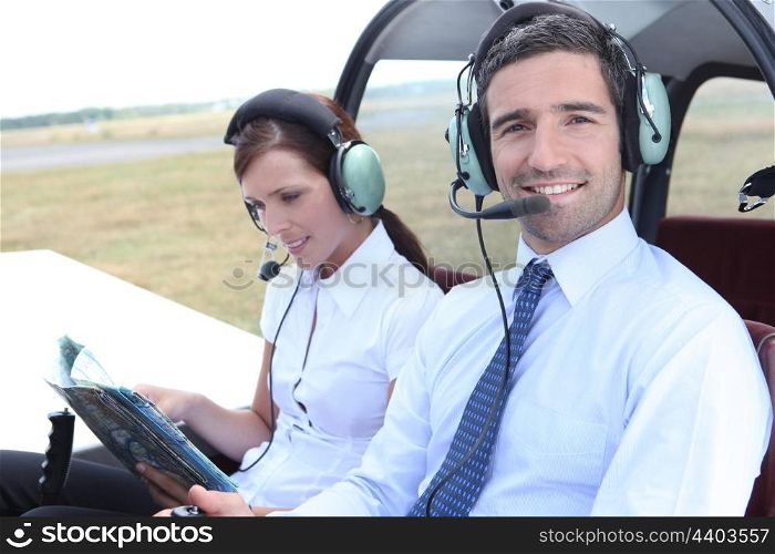 Smiling man sitting in the cockpit of a light aircraft as his partner consults a mapbook