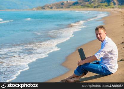 smiling man sitting on the sand beside the sea