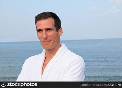 Smiling man standing by the sea in bathrobe