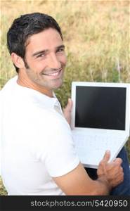 Smiling man using a laptop with a blank screen in a field