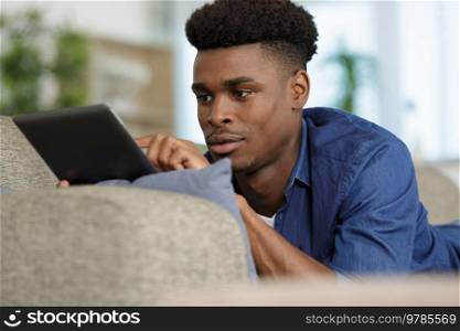 smiling man using a tablet while laying on a sofa