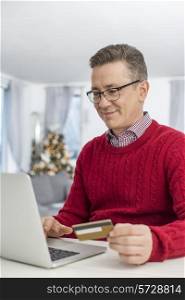 Smiling man using credit card and laptop to shop online at home during Christmas