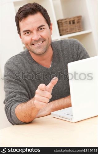 Smiling Man Using Laptop Computer At Home Pointing To Camera