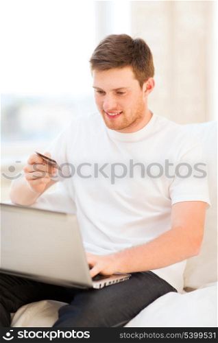 smiling man with laptop and credit card at home