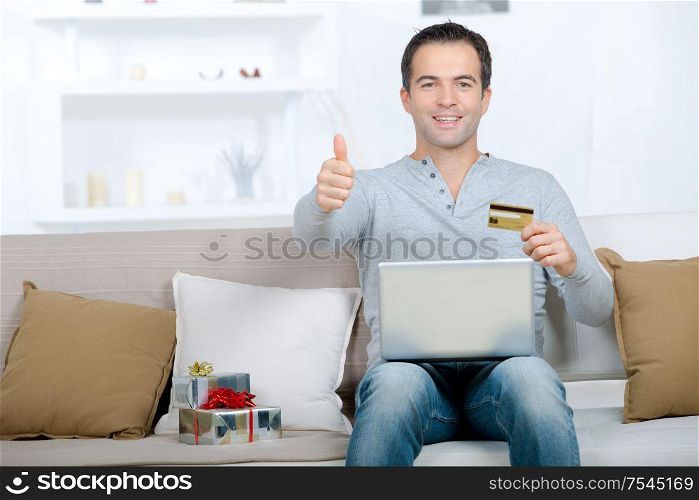 smiling man with laptop and credit card showing thumbs up