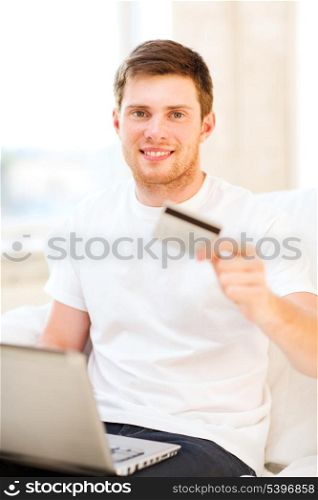 smiling man with laptop showing credit card at home