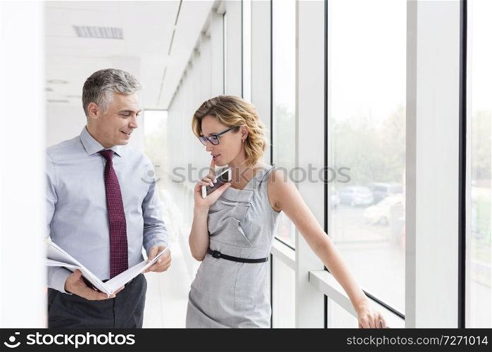 Smiling mature businessman looking at businesswoman while discussing by window in new office