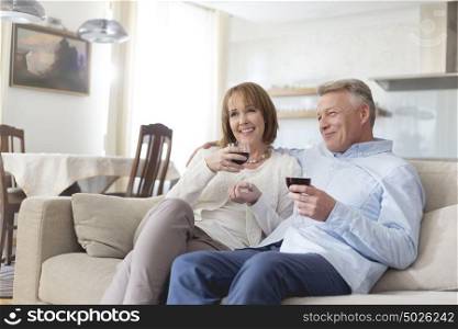 Smiling mature couple sitting on sofa while holding wineglasses at home