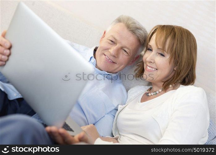 Smiling mature couple using laptop in bedroom at home