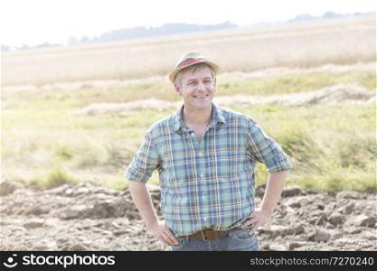 Smiling mature farmer standing with hands on hip at farm