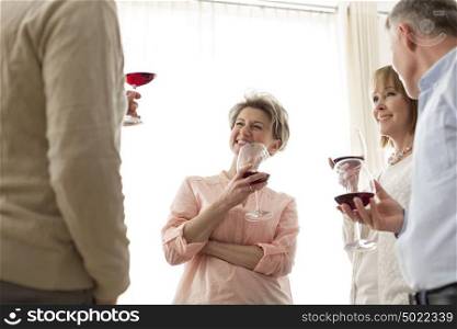 Smiling mature friends standing with drinks at home