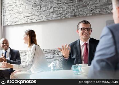 Smiling mature man talking with male colleague in office cafeteria