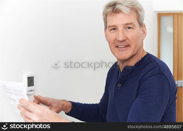 Smiling Mature Man With Bill Adjusting Central Heating Thermostat