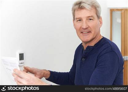 Smiling Mature Man With Bill Adjusting Central Heating Thermostat