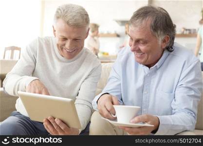 Smiling mature men using digital tablet while sitting on sofa at home