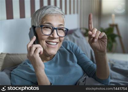 Smiling Mature woman in bed, talking over phone . Smiling Mature Woman Talking Over Phone