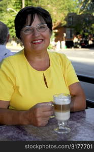 Smiling mature woman in outdoor cafe holding a coffee