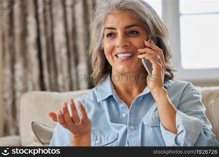 Smiling Mature Woman Making Call On Mobile Phone At Home