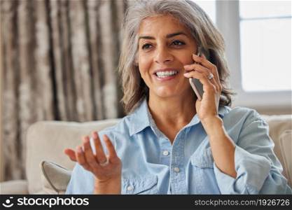 Smiling Mature Woman Making Call On Mobile Phone At Home
