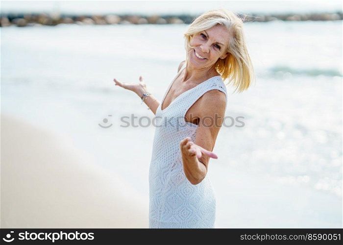 Smiling mature woman opening her arms on a tropical beach. Elderly female enjoying her retirement walking on the beach.. Smiling mature woman walking on the beach, spending her leisure time, enjoying her free time