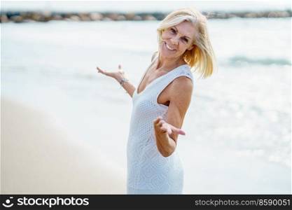 Smiling mature woman opening her arms on a tropical beach. Elderly female enjoying her retirement walking on the beach.. Smiling mature woman walking on the beach, spending her leisure time, enjoying her free time