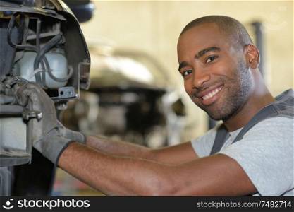 smiling mechanic fixing a car engine in his garage