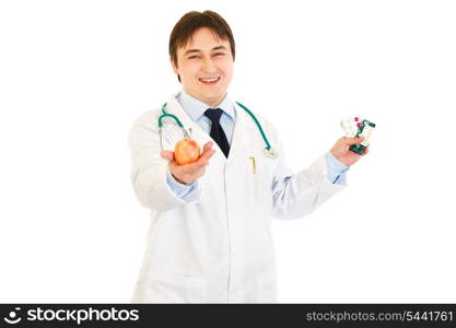 Smiling medical doctor giving apple and holding packs of pills in other hand isolated on white. Concept: healthy eating - illness prevention&#xA;