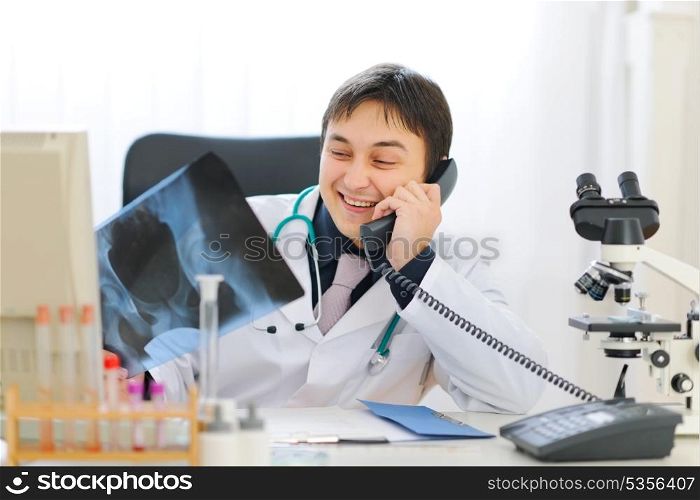 Smiling medical doctor holding patients roentgen and speaking phone