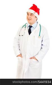 Smiling medical doctor in hat of Santa Claus looking up at copy space isolated on white&#xA;