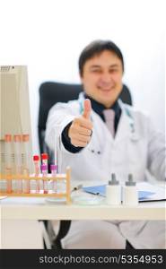 Smiling medical doctor showing thumbs up. Focus on hand