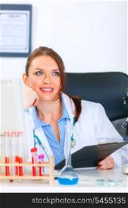 Smiling medical doctor woman sitting at office table and looking in corner&#xA;